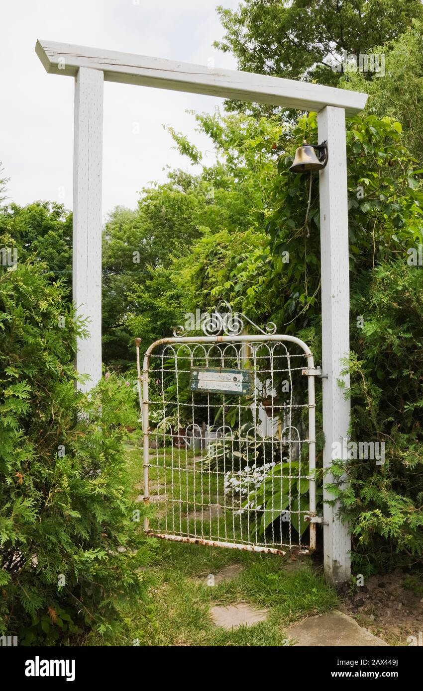White wooden arbour with rusted metal fence gate flanked by Thuja occidentalis - Cedar trees in backyard garden in summer Stock Photo