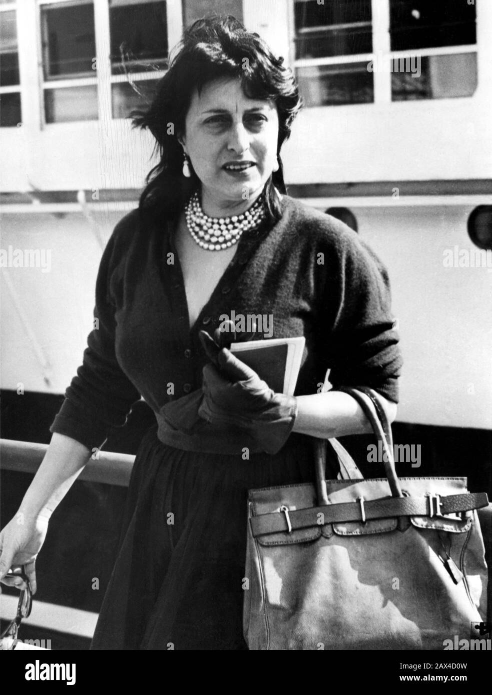 1953 , 4 april , NAPLES , ITALY : The italian movie actress ANNA  MAGNANI before sailing on the italian liner ANDREA DORIA from Napoli to USA . Magnani was on the way to USA where she will help to publicize her latest film  THE GOLDEN COUCH ( La carrozza d'oro - La Carosse d'or ) by Jean Renoir  - CINEMA - FILM -  MOVIE - PORTRAIT - RITRATTO  - black dress - abito vestito nero - pearls necklace - collana di perle - gloves - guanti - borsa - borsetta - sac - bag - orecchini - eardrops - TRANSATLANTICO  --- ONLY EDITORIAL USE --- NOT FOR ADVERTISING USE --- NON PER USO PUBBLICITARIO ---  Archivi Stock Photo