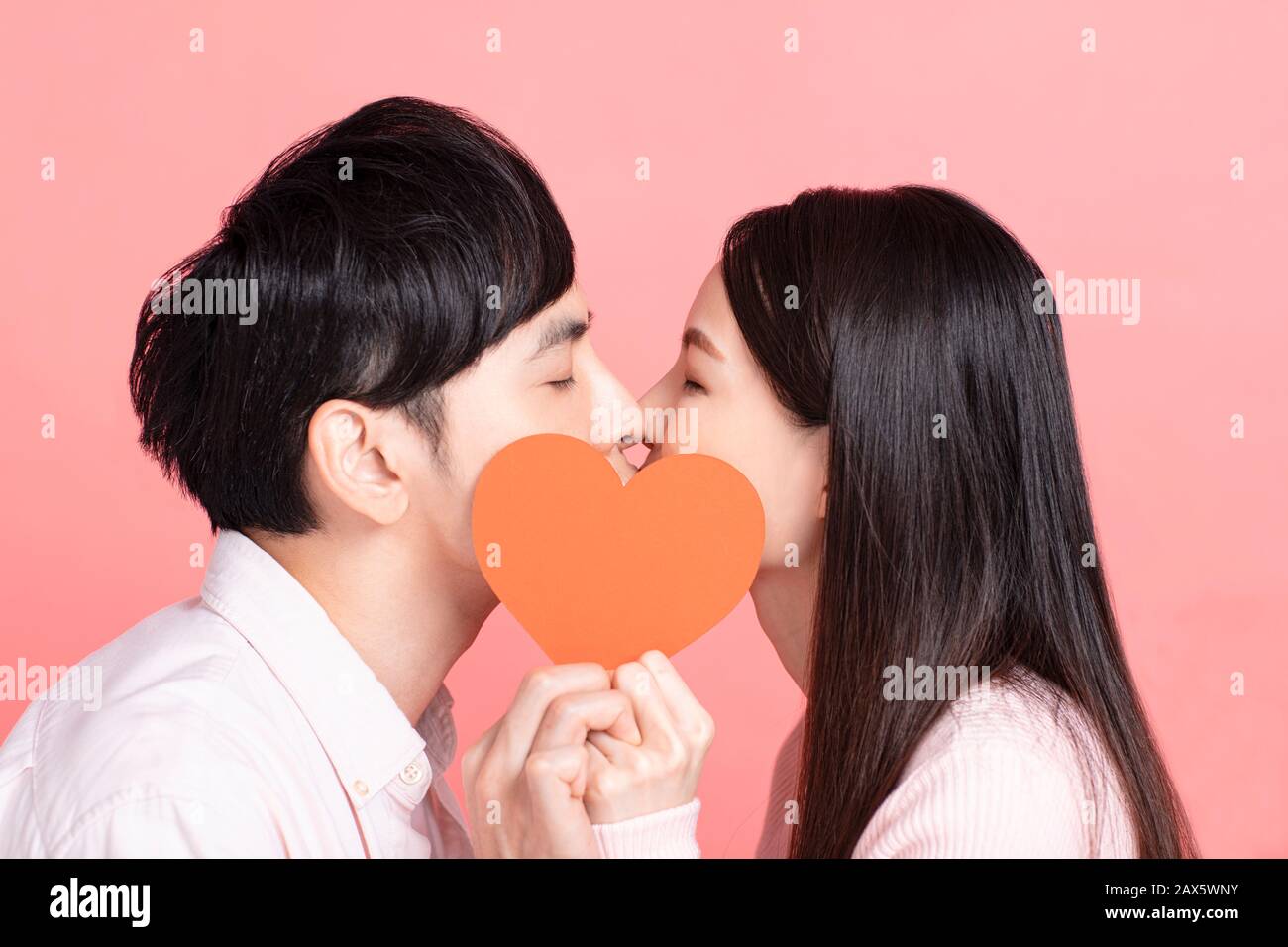 Happy young couple holding red paper hearts and kissing Stock Photo - Alamy
