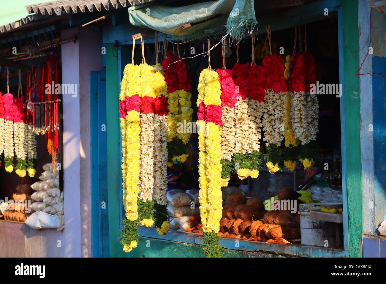 close up shot of multicolored marigold flowers, rose flowers, jasmine flowers and green betel leaf garland hanging on rod in street shop on market ,st Stock Photo