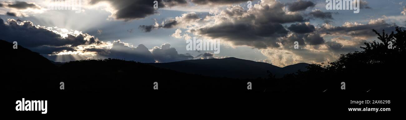 Sunset above the mountains with sun rays breaking through the clouds. Stock Photo