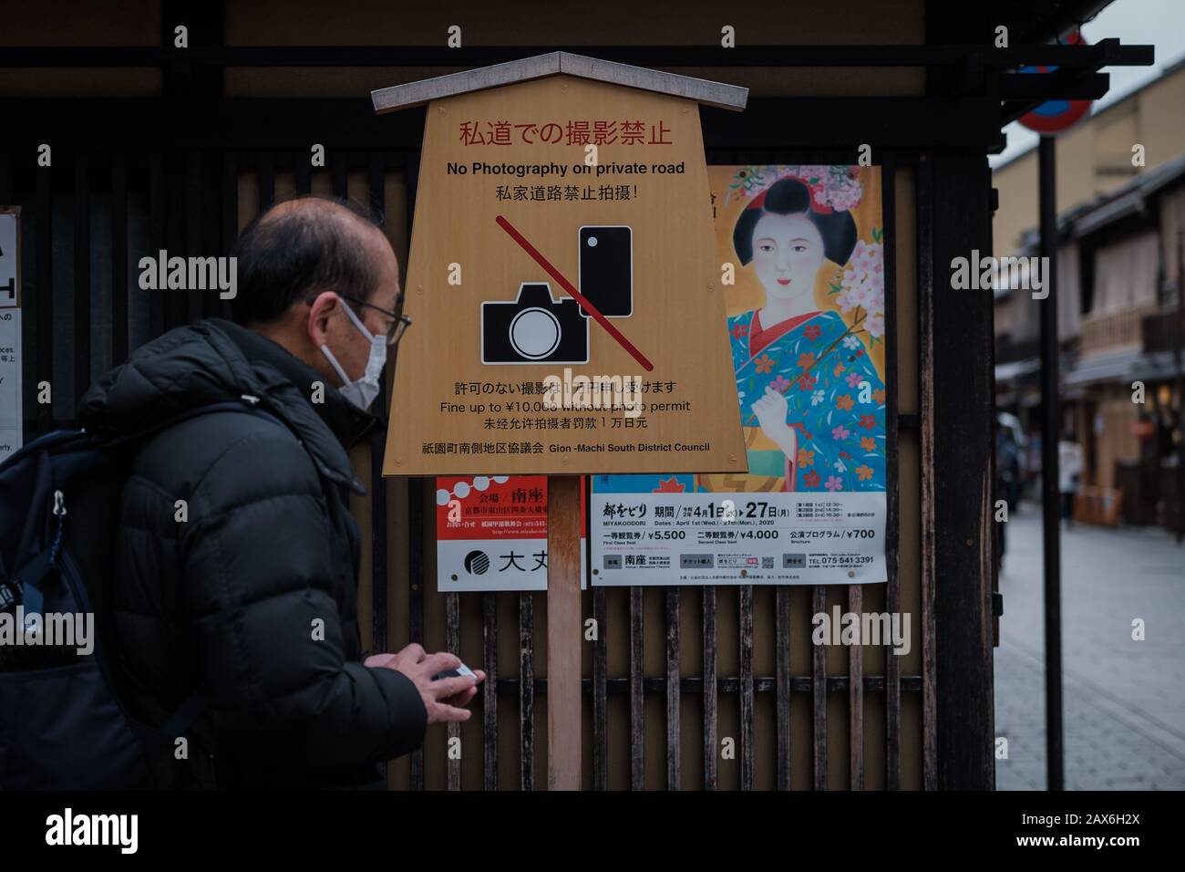 A man wearing a mask passes by a board sign banning photography and poster of geisha on Hanamikoji Street on February 10, 2020. The boorish behavior of tourists who have harassed geisha, destroyed property and committed other obnoxious acts has led to a ban on photography on private roads in Kyoto's famed Gion district.Following the outbreak of Coronavirus situation many chinese tourists cancelled trip in Japan during winter. The city is empty of bus and tourist's groups. February 10, 2020 Credit: Nicolas Datiche/AFLO/Alamy Live News Stock Photo