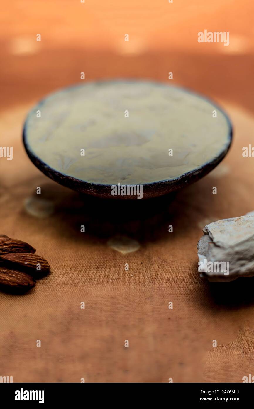 Fuller's earth face mask in a clay bowl on brown fabric's surface along with some milk and almonds. For softer skin. Stock Photo