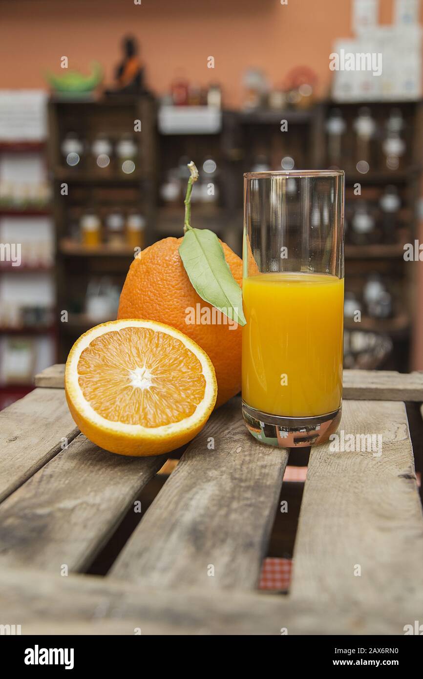 Vertical shot of a glass of orange juice and fresh oranges on a wooden crate with blurry background Stock Photo