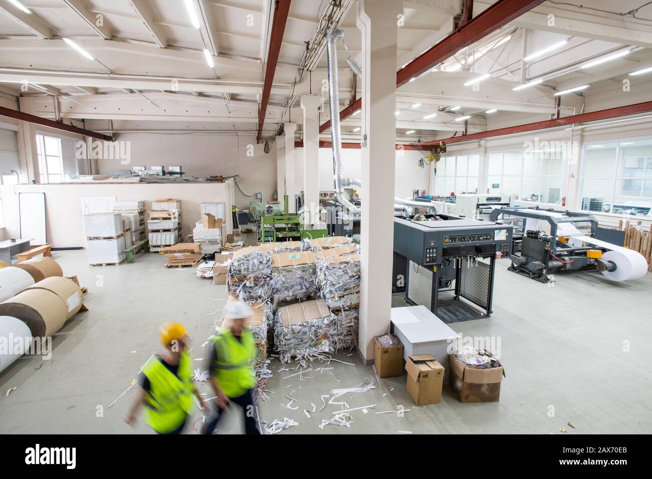 Interior of printing house with packaged paper garbage, printing machines and paper rolls, blurred motion of workers Stock Photo