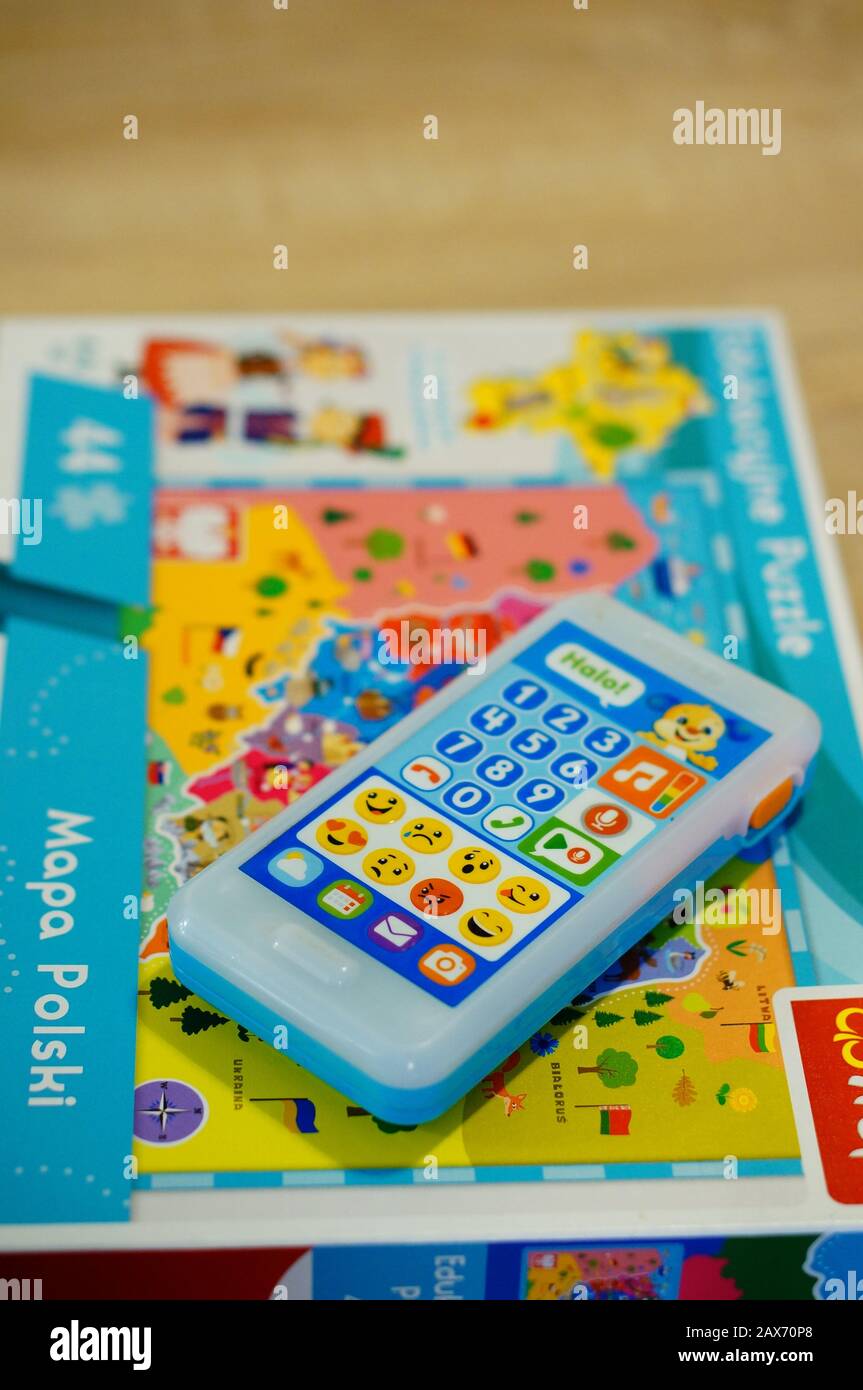 POZNAN, POLAND - Feb 02, 2020: Plastic Fisher Price toy phone laying on a puzzle box in soft focus background. Vertical high angle view. Stock Photo
