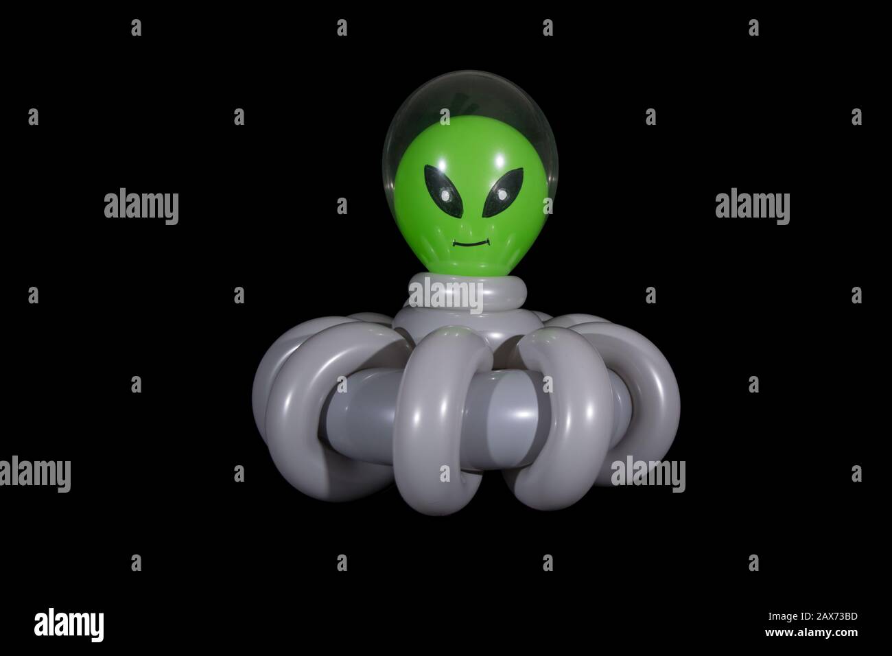Inflated balloon twisting sculpture of an alien inside the clear cockpit of a gray spaceship flying through outer space with a black background. Stock Photo