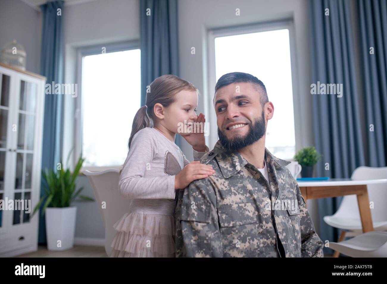 Little daughter whispering in the ear of her dad. Stock Photo