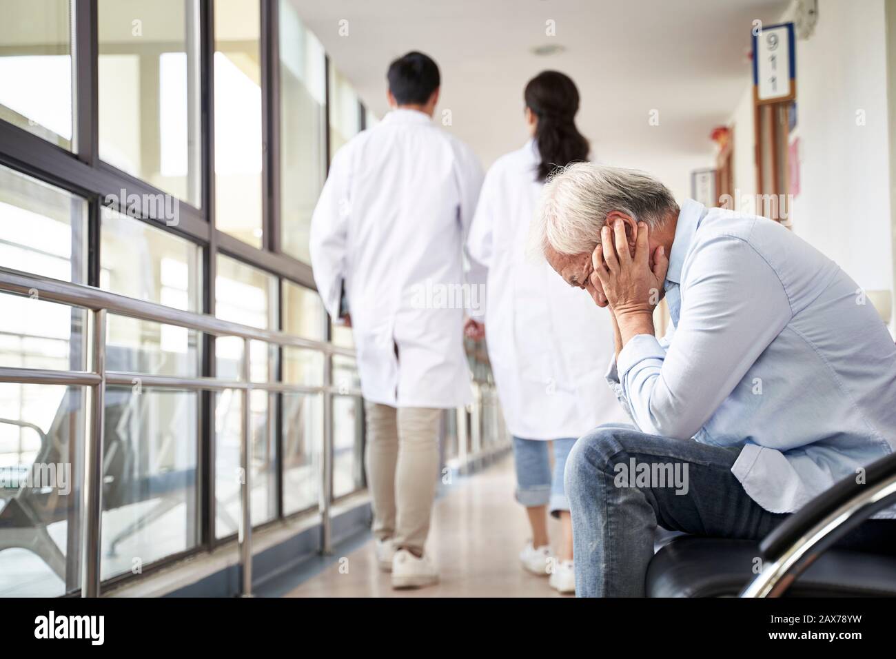 asian old man sitting in hospital hallway looking sad and depressed Stock Photo