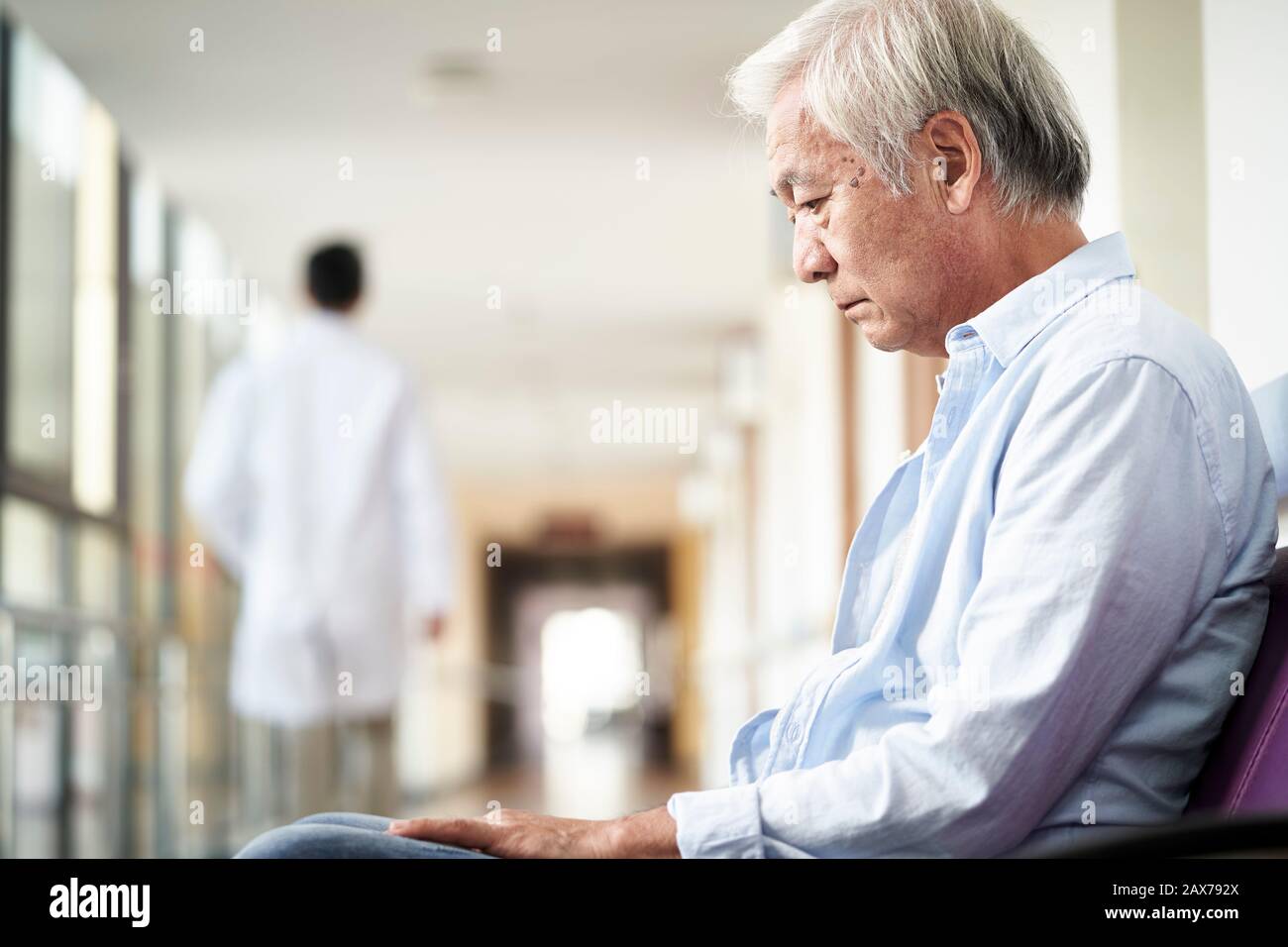 asian old man sitting in hospital hallway looking sad and depressed Stock Photo