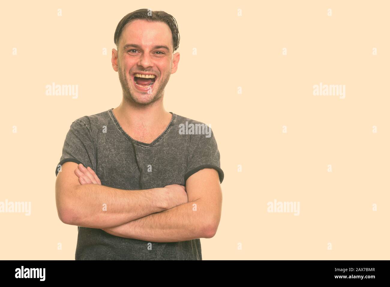 Studio shot of young happy man smiling and laughing with arms crossed Stock Photo