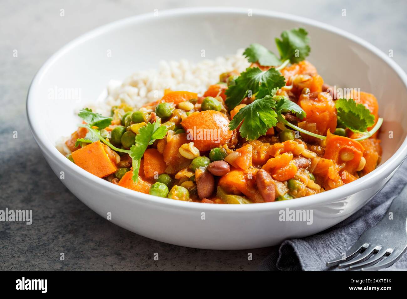 Vegan curry with rice in a white bowl. Curry with sweet potato, peas and beans in a plate with rice. Stock Photo