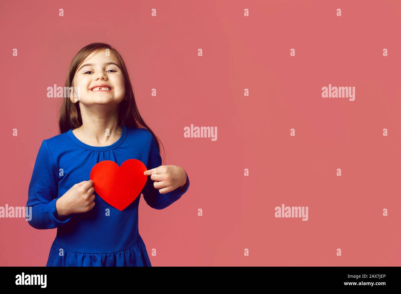 Funny smiling little girl delighted with received valentines. Blue dress and red heart. Copy space. Valentine's day concept, love for all ages. Stock Photo