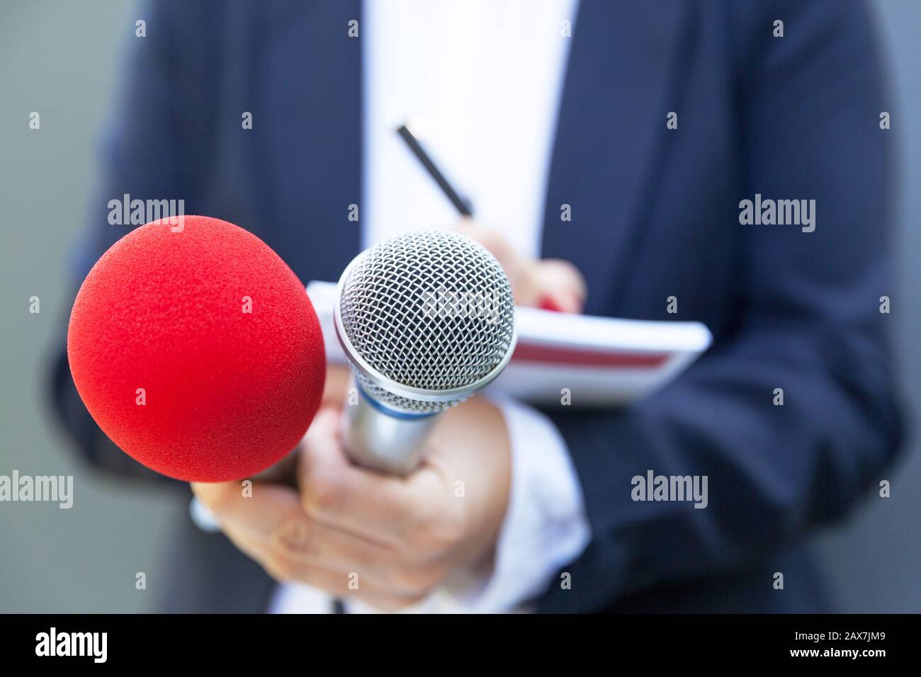 Female reporter at press conference, writing notes, holding microphone ...