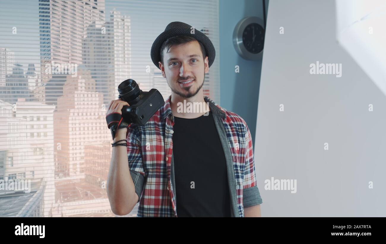 Portrait of young professional photographer in casual clothes with his camera smiling and posing. There are skyscrapers in the background. Stock Photo