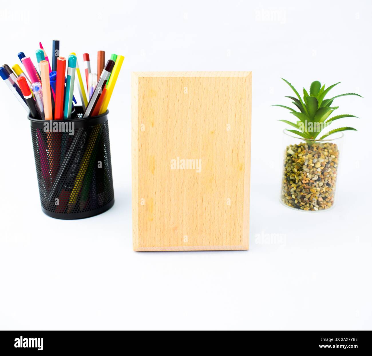 Wooden plaque which is with a black pencil holder full of crayons and a miniature tree on a white background Stock Photo