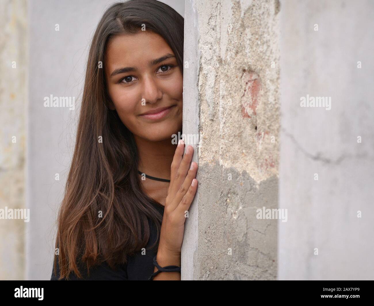 Young woman with beautiful hair looks around the corner of an old house. Stock Photo