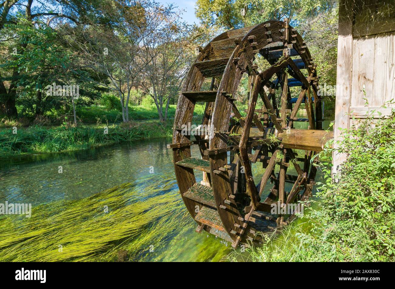 Water mill wheel on river on sunny day. Sustainable energy and water power traditional machinery Stock Photo