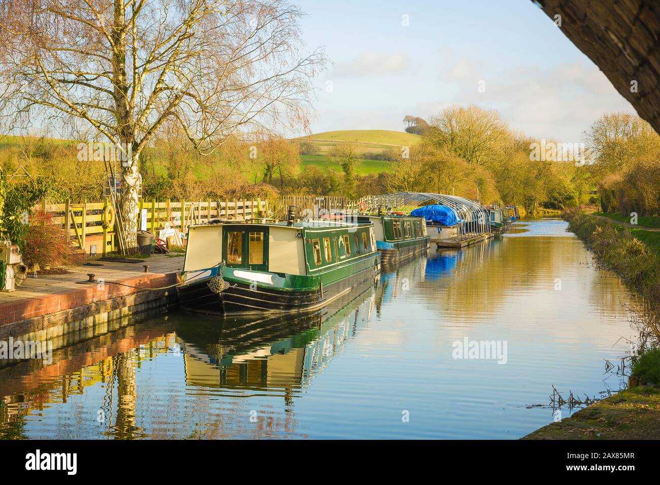 A calm sunny landscape in early January showing the Kennet and Avon canal and narrow boats moored at Honeystreet in the Vale of Pewsey in Wiltshire England UK Stock Photo