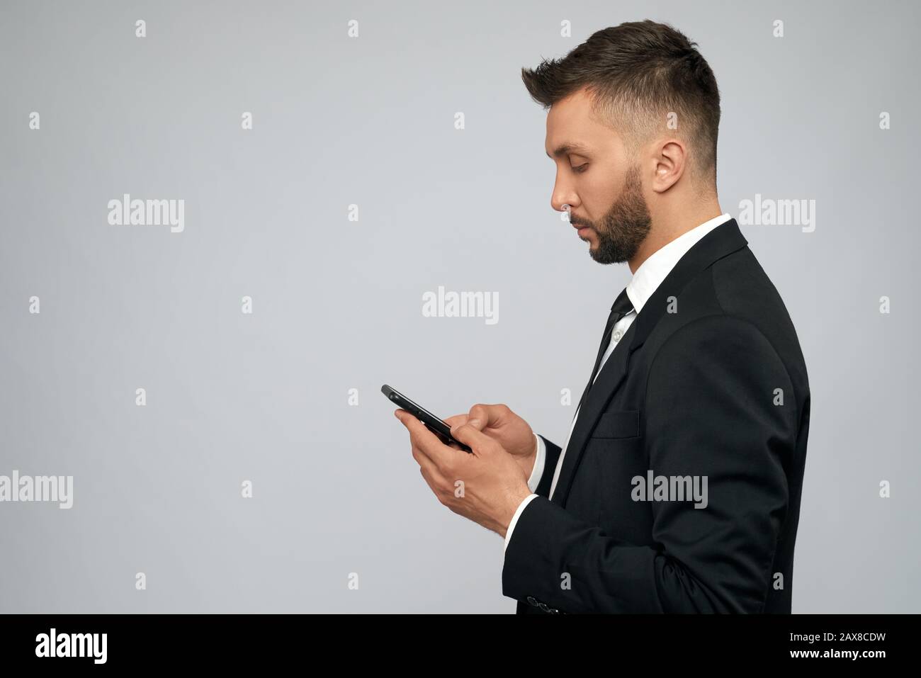 https://c8.alamy.com/comp/2AX8CDW/side-view-of-young-brunette-businessman-in-black-formal-suit-typing-on-smartphone-in-office-handsome-serious-bearded-man-working-using-gadget-isolated-on-grey-concept-of-gadgets-business-2AX8CDW.jpg