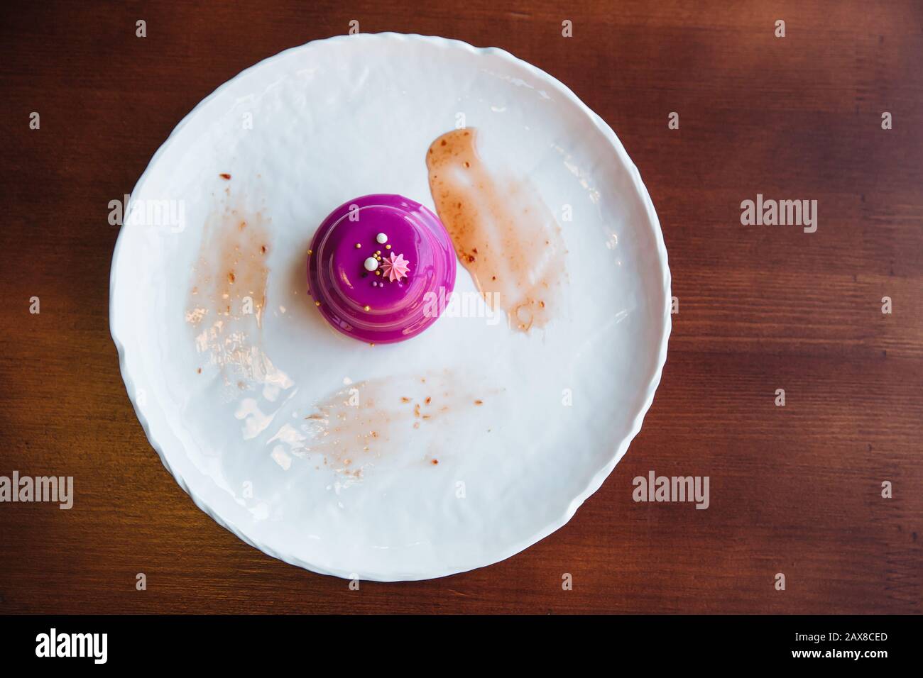Round cake with walnut filling poured pink glaze. On a white plate, standing on the table. Stock Photo