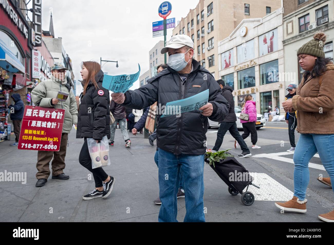 A Chinese American man wearing a surgical mask hands out Chinese language advertising flyers on Main St. & Roosevelt Ave. in Chinatown, Flushing, NYC. Stock Photo