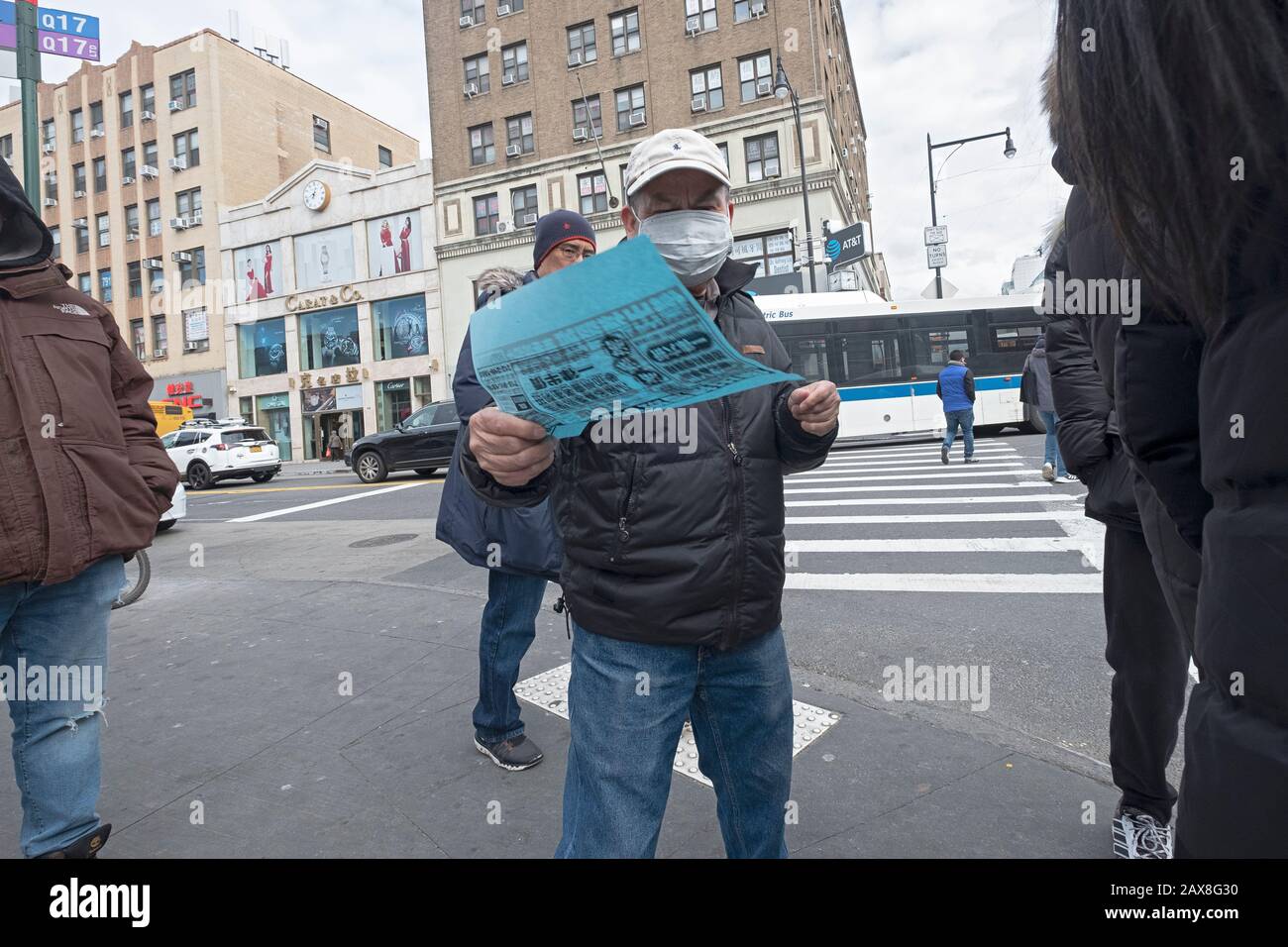 A Chinese American man wearing a surgical mask hands out Chinese language advertising flyers on Main St. & Roosevelt Ave. in Chinatown, Flushing, NYC. Stock Photo