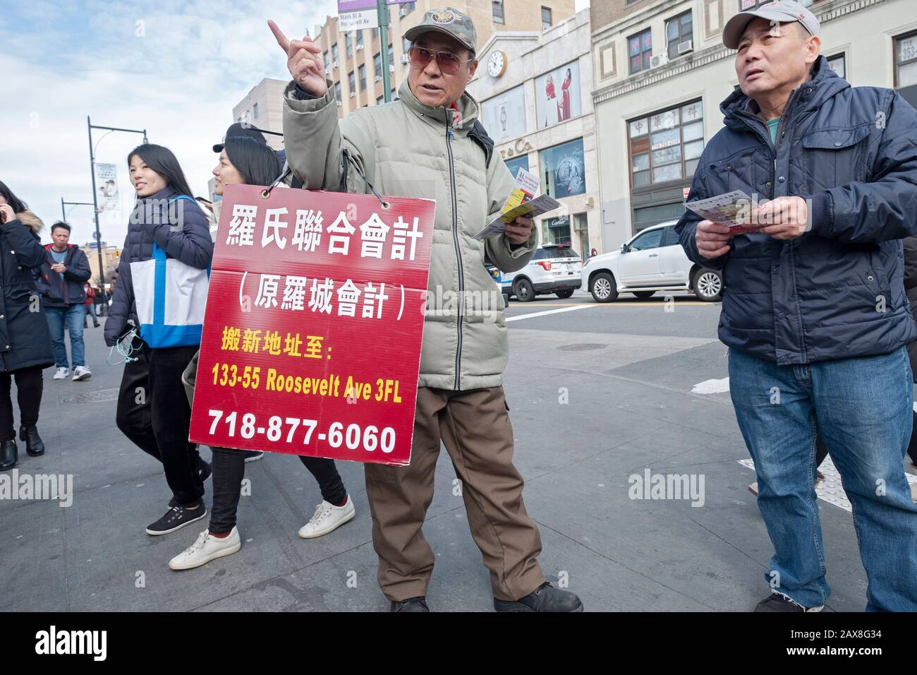 A man who hands out flyers for an electronics store directs a shopper to its location. In Chinatown, Flushing, Queens, New York City. Stock Photo