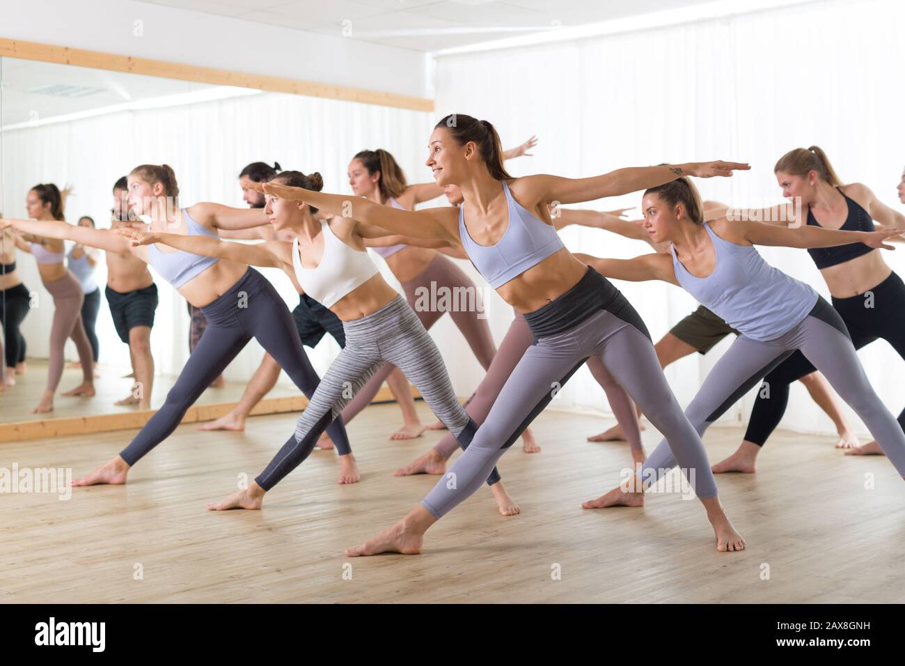 Group of young authentic sporty attractive people in yoga studio, practicing yoga lesson with instructor. Healthy active lifestyle, working out in gym Stock Photo