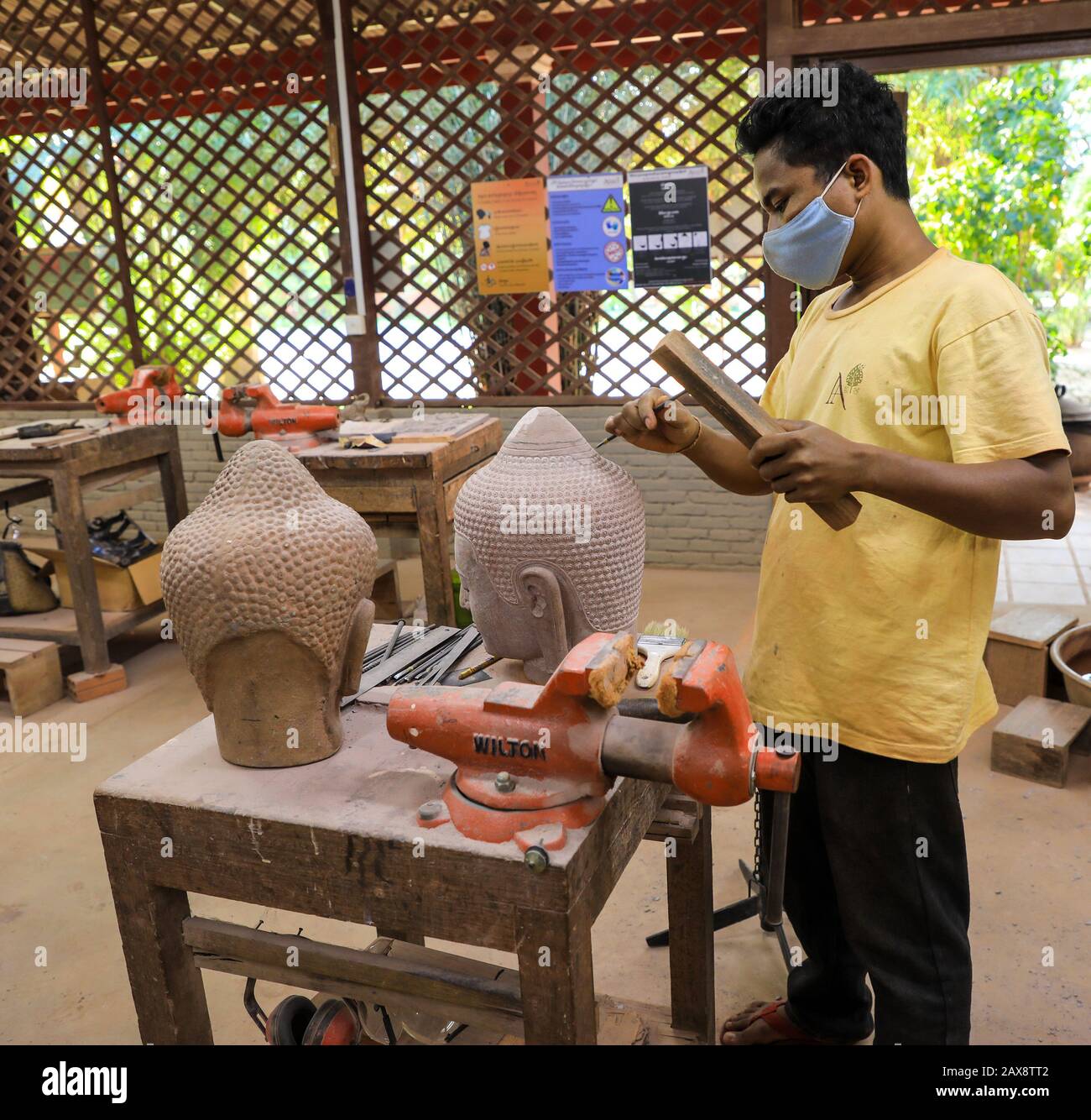 A man using a chisel to carve stone heads at Artisans d'Angkor, a worker co-operative workshop, Siem Reap, Cambodia Stock Photo