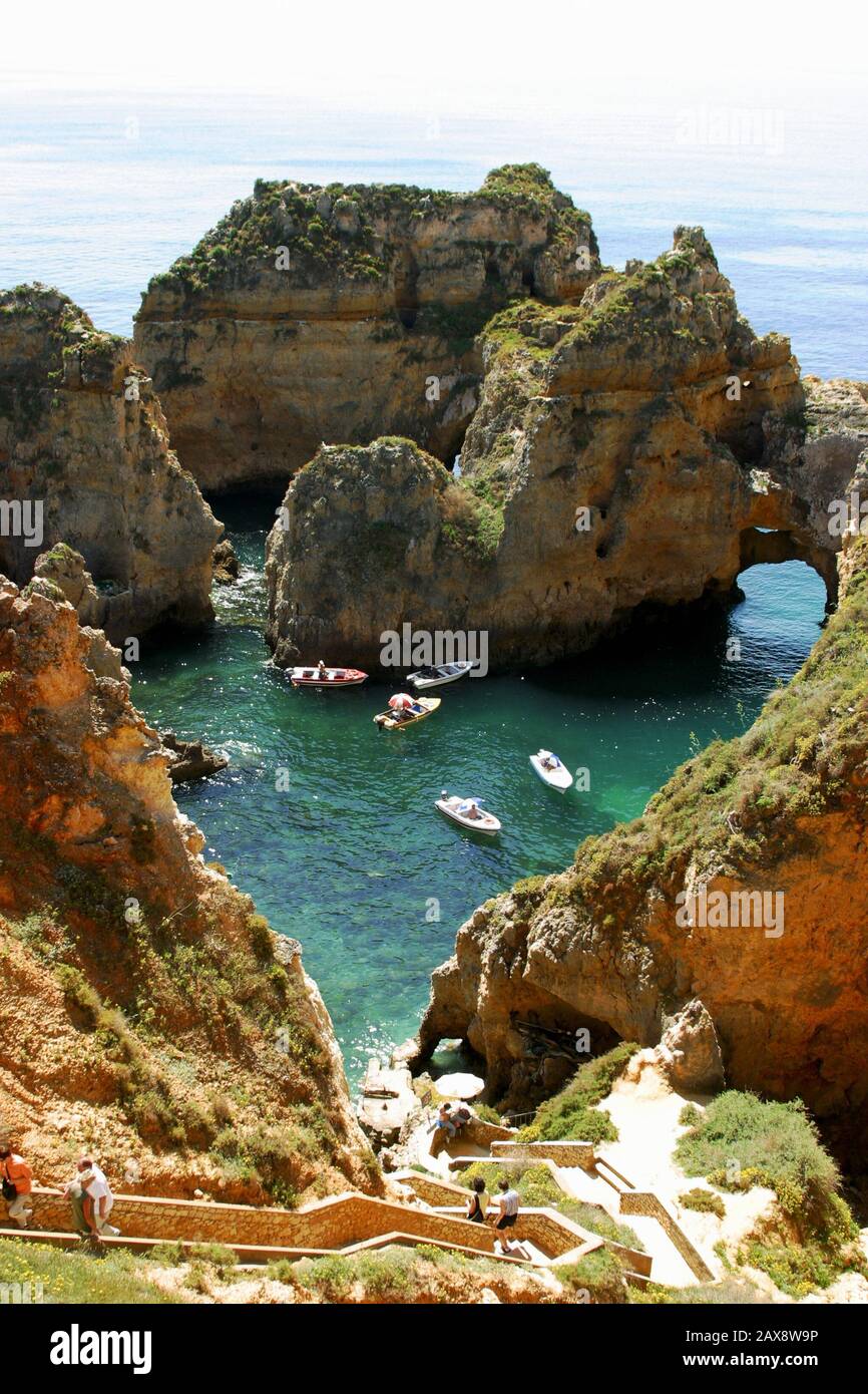 Tourist boats gathering in a cove surrounded by rocks, accessed by a cave-like fairway Stock Photo