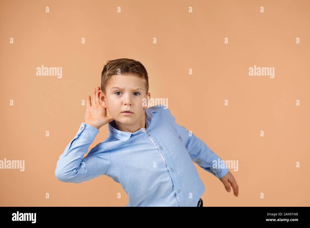 happy little child boy in shirt making hearing gesture . facial expression. kid with hand over ear listening gossip. Stock Photo
