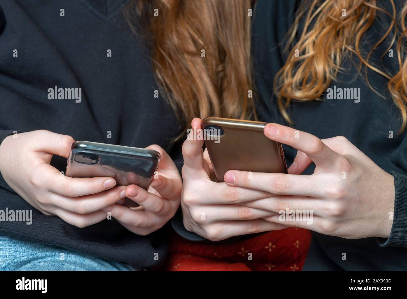 teenage girls being cyber bullies  or just catching up on social media both on there phones, hand level  copy space above Stock Photo