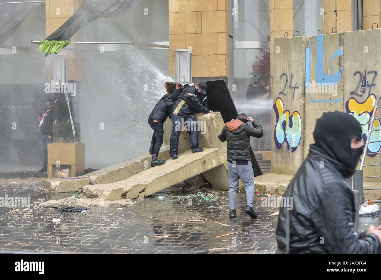 Downtown Beirut, Lebanon. 11th Feb, 2020. protesters take shelter behind building site hordings as police fire water canon at them. People gathered to protest at barriers preventing them from reaching parliament on the day of a vote of confidence in the new cabinet proposed by interim PM, Hassan Diab. Credit: Elizabeth Fitt/Alamy Live News Stock Photo