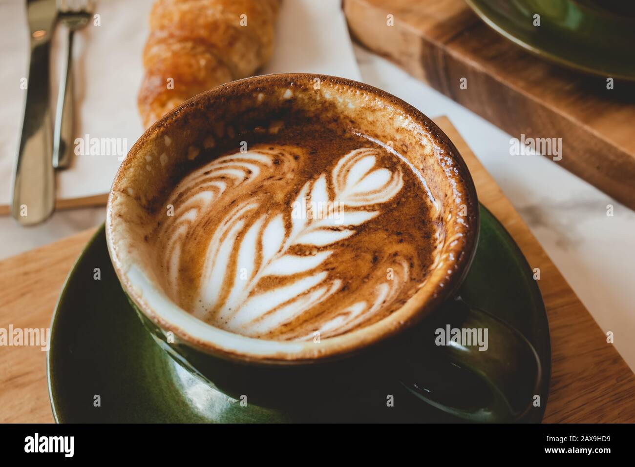 Hot coffee cappuccino latte art serve with croissant in morning worm lighting. Stock Photo