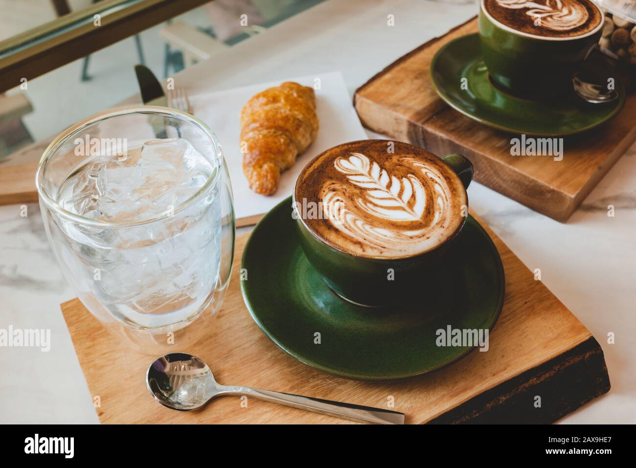 Hot coffee cappuccino latte art serve with croissant in morning worm lighting. Stock Photo