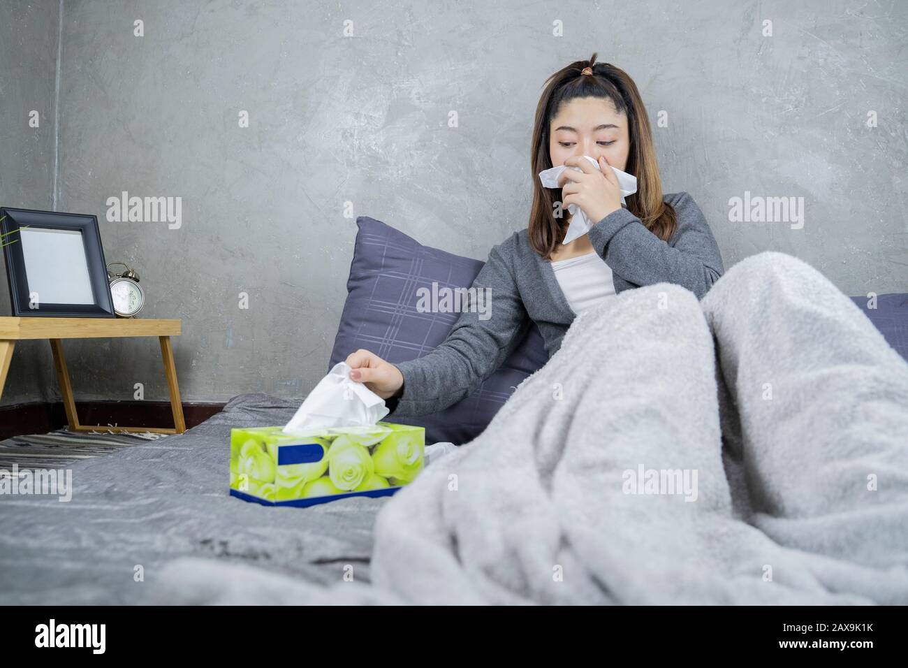 Sick day at home. Asian woman has runny nose and common cold. Cough. Beautiful Young Woman Caught Cold Or Flu Illness. Stock Photo