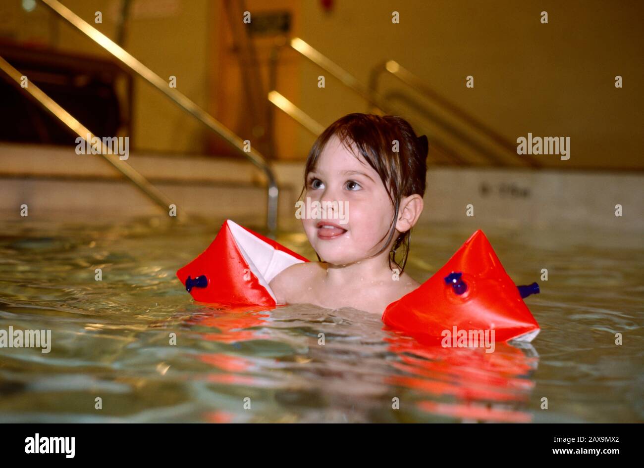young girl wearing armbands learning to swim in a swimming pool Stock