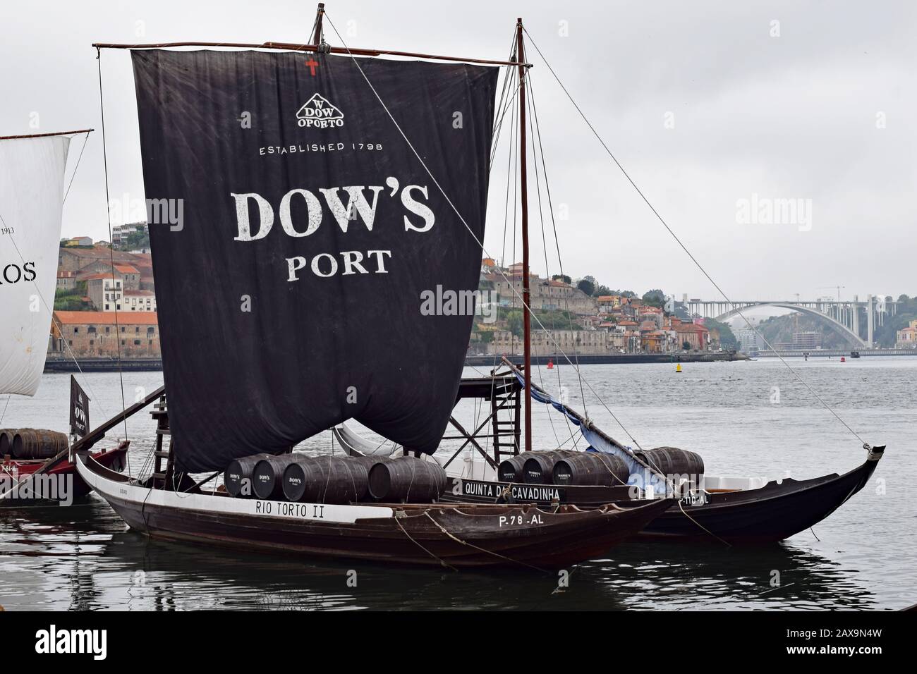 Dow's port rabelo boat moored on the riverside of the Douro river in Gaia Porto. Black sail raised and billowing with Porto and bridge in background Stock Photo