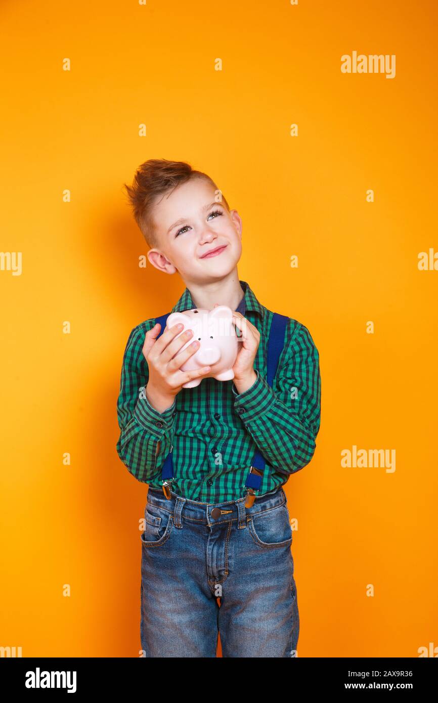 Little boy holding a piggy bank in his hands on yellow background Stock Photo