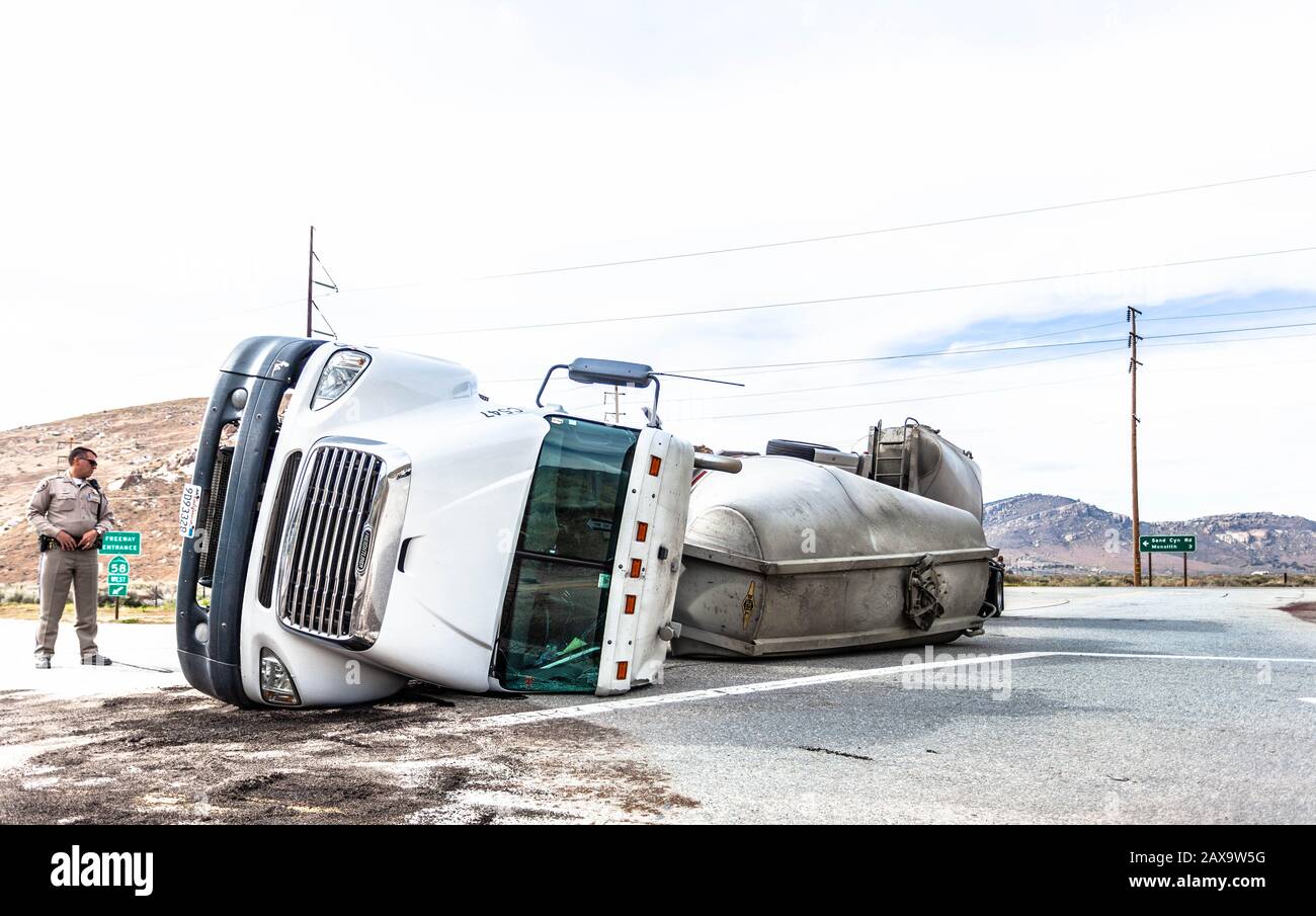 A deputy sheriff officer stands next to an overturned fuel tanker truck in the middle of a road, California, USA. Stock Photo