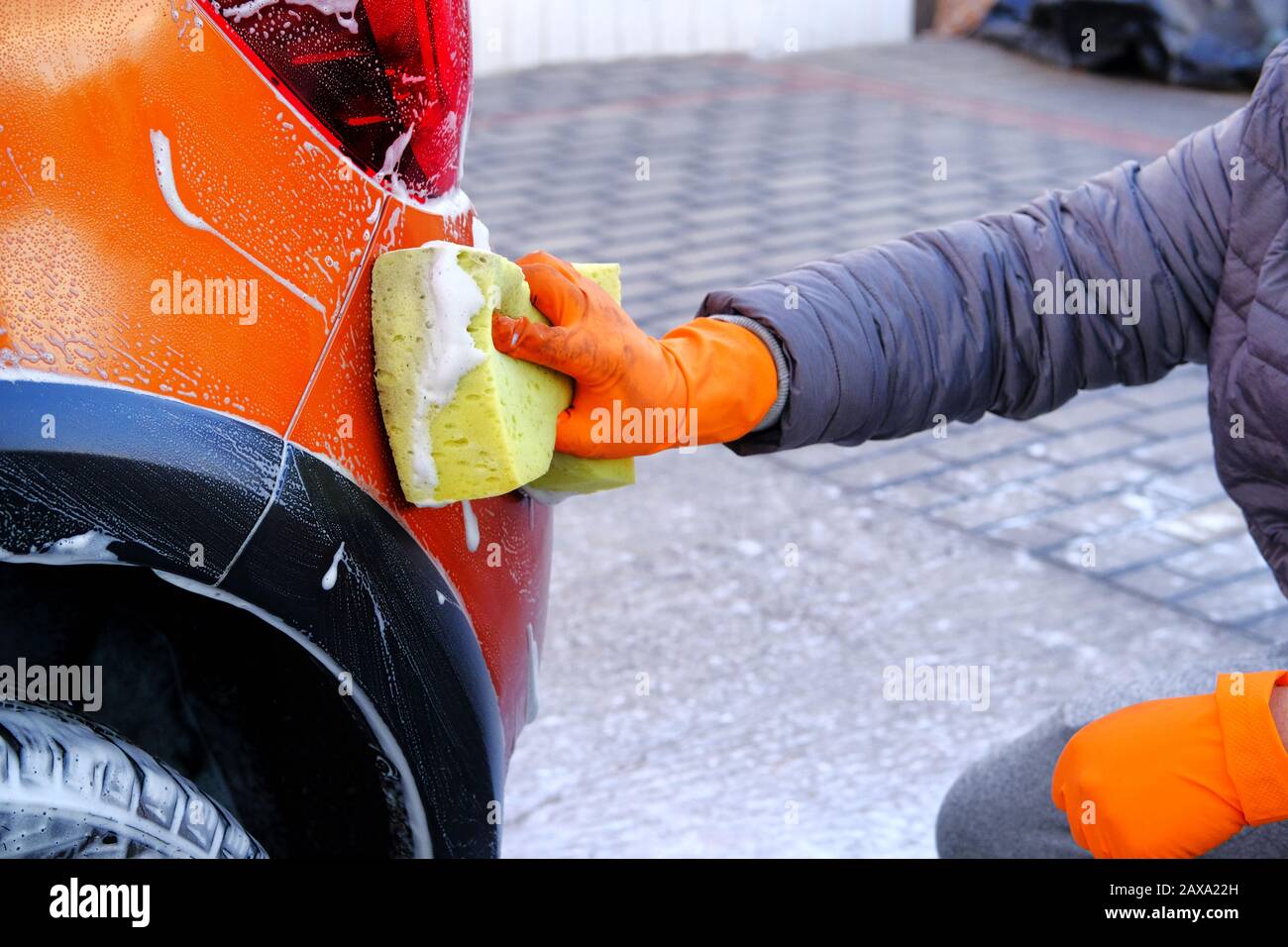 Cleaning with white soap suds at self-service car wash. Man in rubber gloves  washes his auto with yellow sponge. Male hand and orange car body closeup  Stock Photo - Alamy