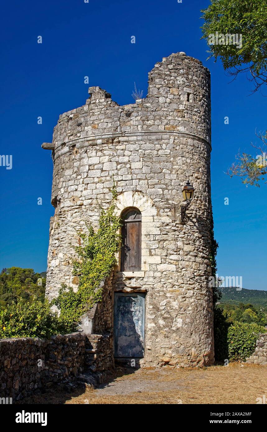 Medieval stone tower, old, abandoned, crumbling, 2 wood doors, low stone wall, Viviers, France; summer, vertical Stock Photo