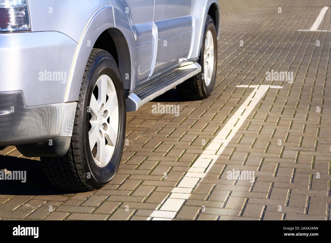 Silver car is parked in its parking spot in city. Close up car wheel, urban environment. Stock Photo