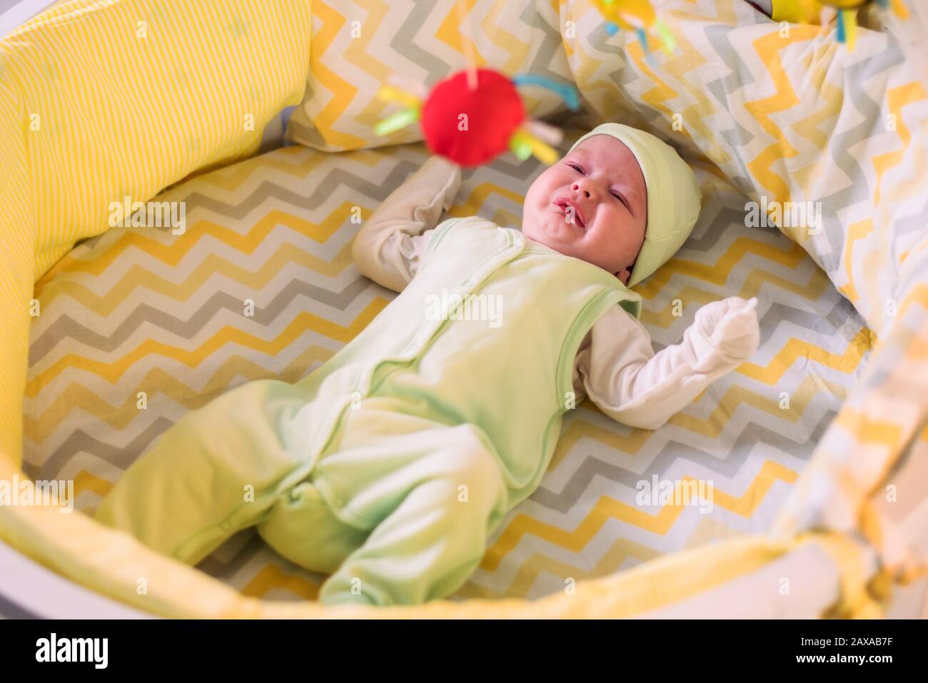 a cute baby is lying in a crib and crying because of colic Stock Photo