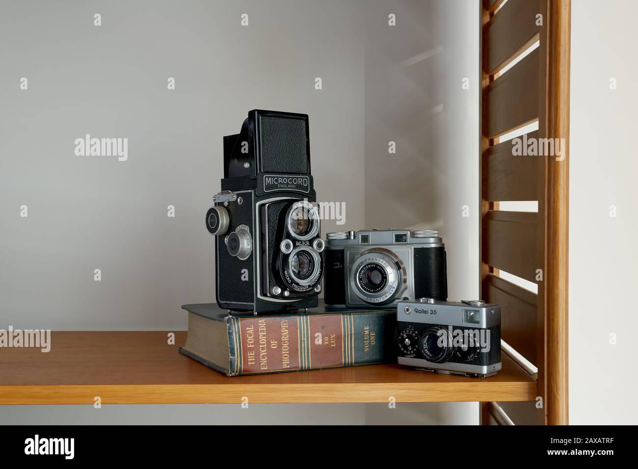 A photograph of three vintage cameras and a vintage photography book placed on a shelf. Stock Photo