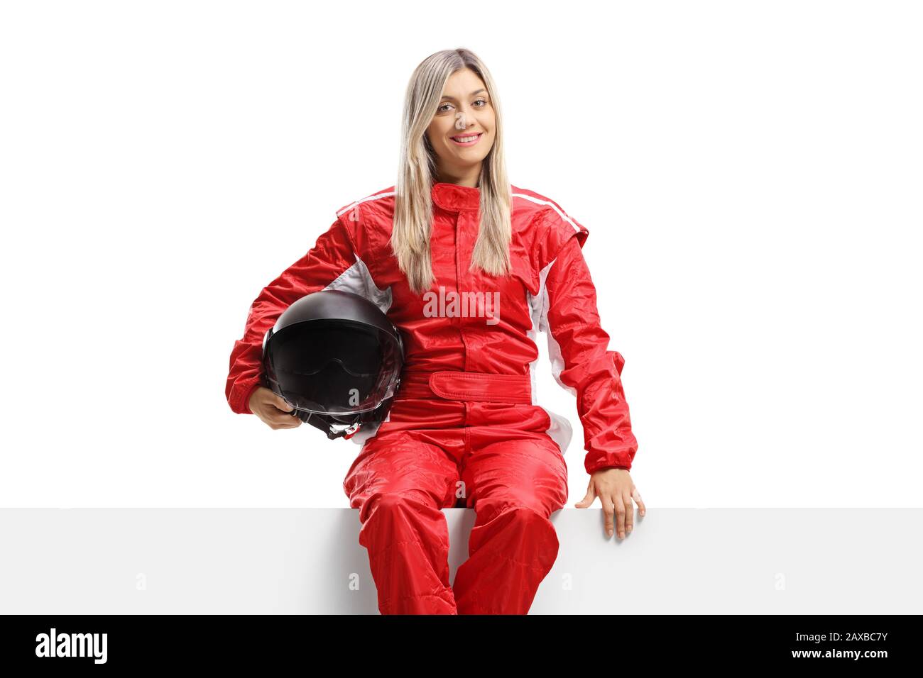 Female racer in a suit holding a helmet and sitting on a panel isolated on white background Stock Photo