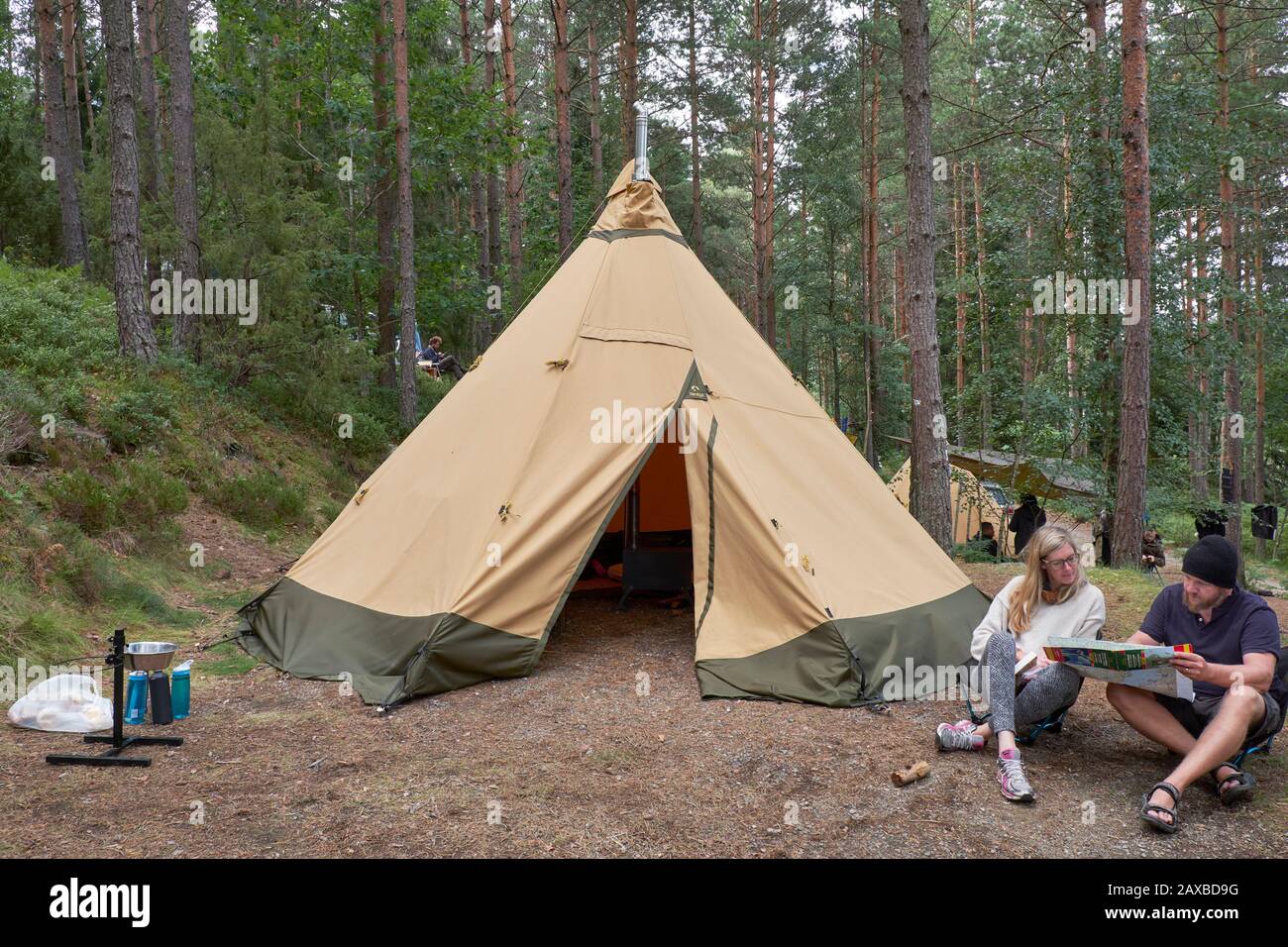 Male and female couple reading a map outside their wigwam shaped tent on forest campsite Stock Photo