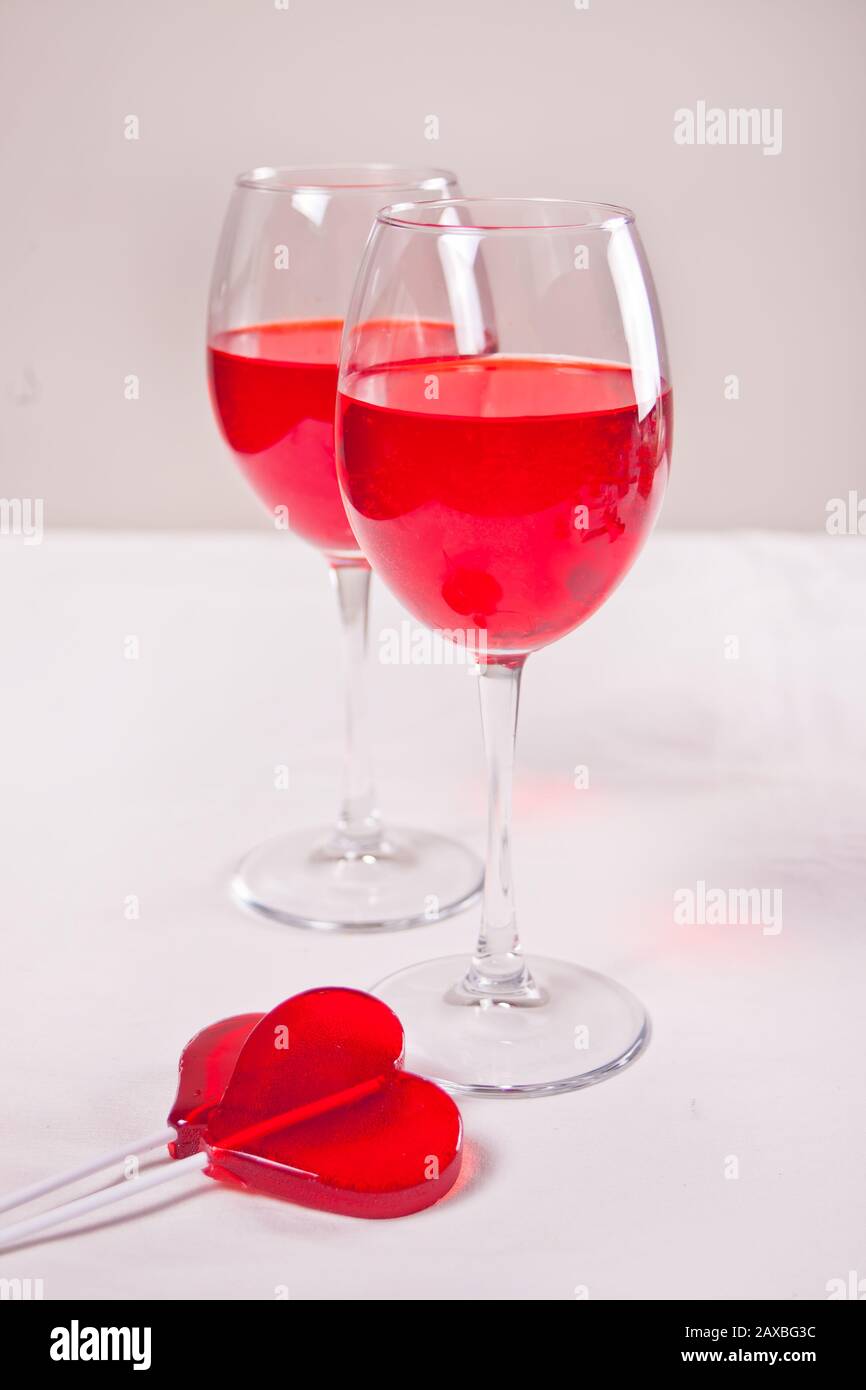 Glasses of red grape wine with red candies heart shape on the white