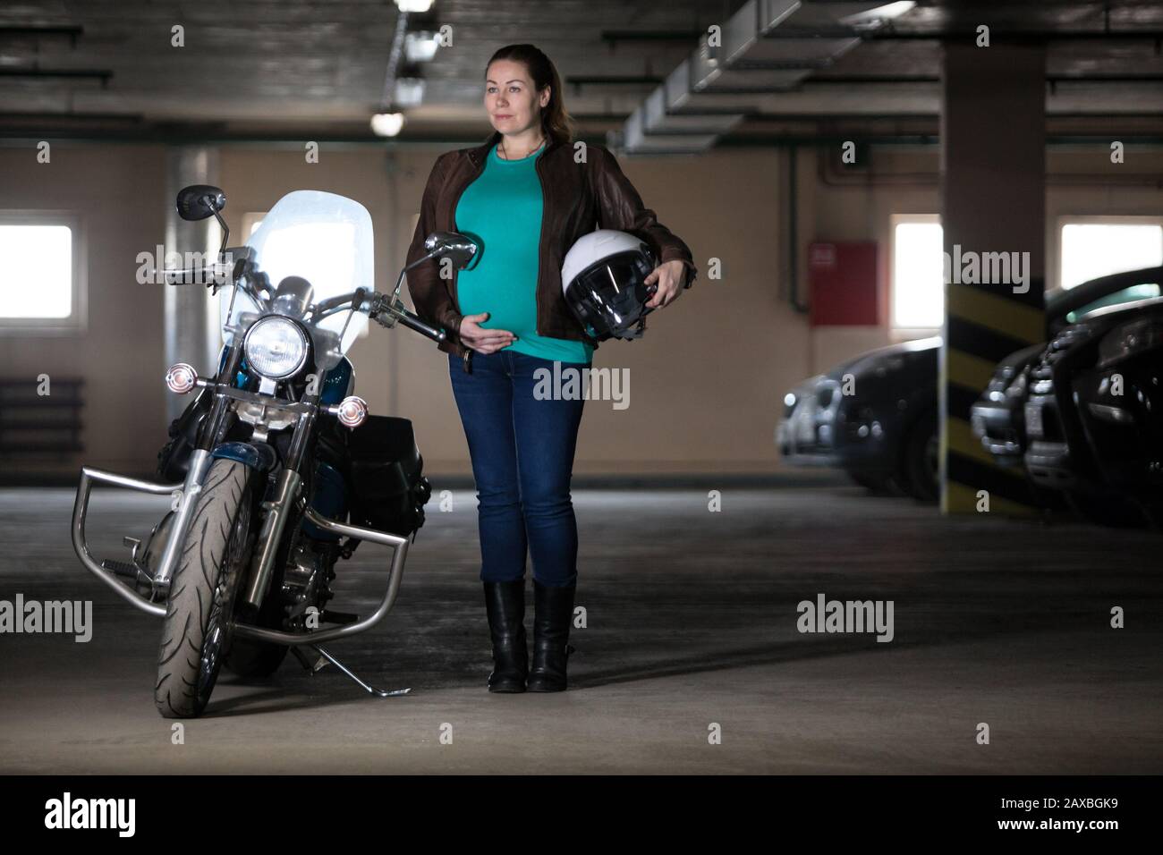 Portrait of pregnant woman biker standing next to motorcycle with white